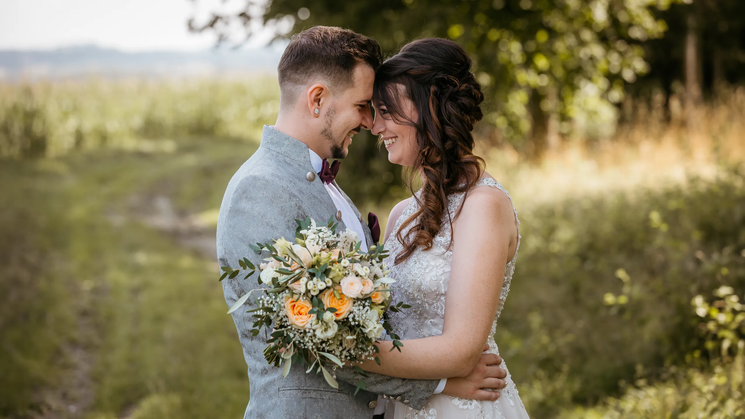 Brautpaar mit Brautstrauß Stirn an Stirn im Grünen – Hochzeitsfotograf in Niederbayern