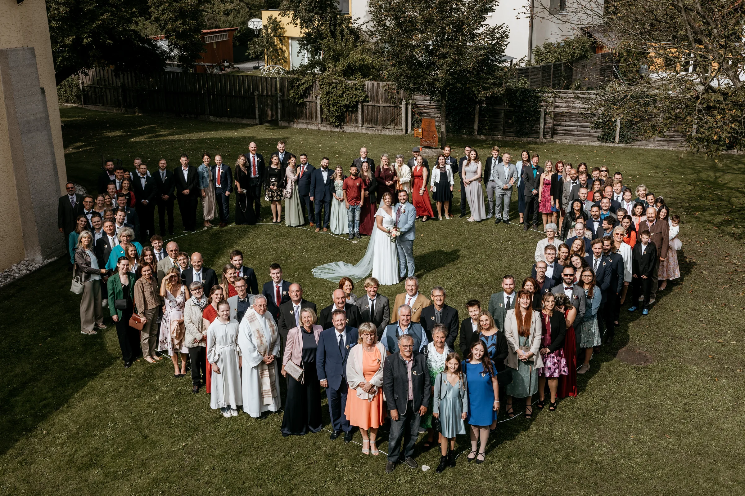 Hochzeitsgäste bilden ein Herz um das Brautpaar – Gruppenfoto bei einer Hochzeit in Bayern