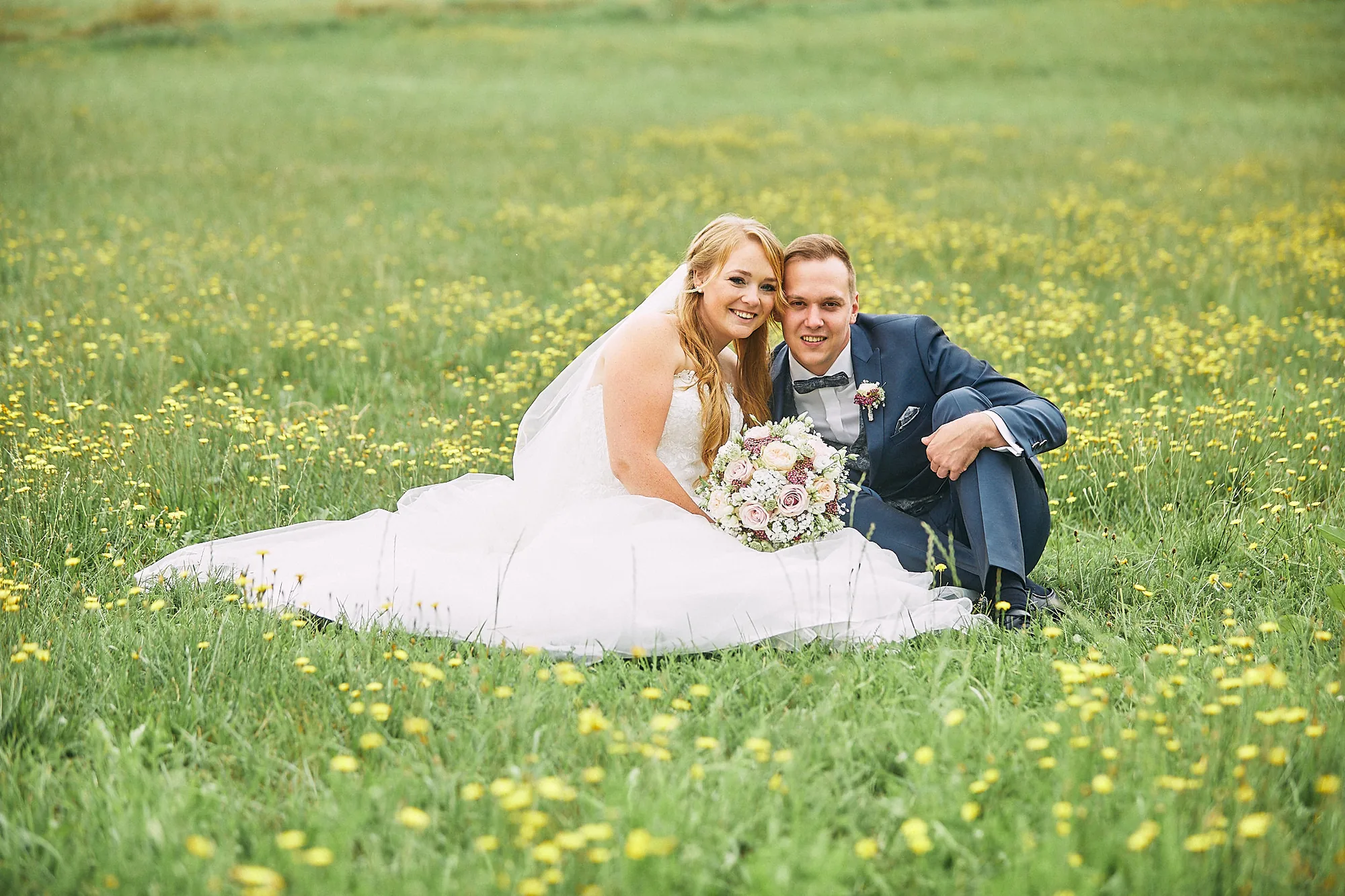Brautpaar sitzt in einer blühenden Blumenwiese – Hochzeitsfotos von Reinhard Fürstberger
